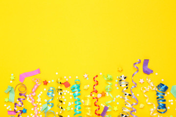 Colorful ribbons with paper stars and confetti on yellow background