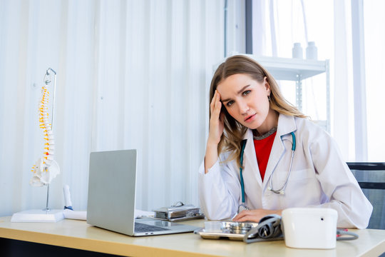 Stressed female doctor with stethoscope have headache working with laptop computer on wooden table in Hospital background - Powered by Adobe