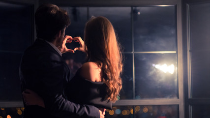 Happy man and woman making heart with hands, back view