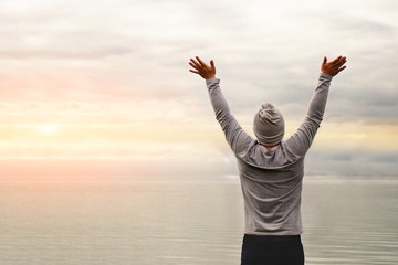 A young man is standing on the shore. The view from the back. Yoga classes. Hands raised up. Freedom and achievement.