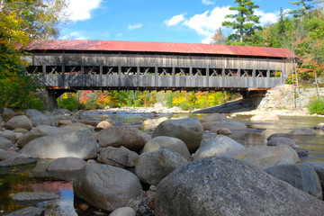 Fototapeta na wymiar Old New England covered bridge over river. Reflection of bridge in water during autumn season