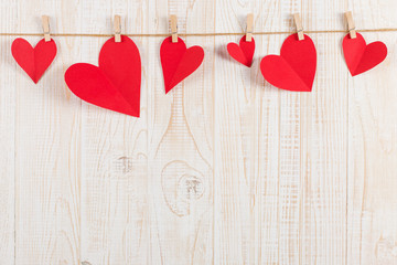 The concept of the preparation for Valentine's Day. Red hearts are held by clothespins on jute rope, on a white wooden background. Copy space.