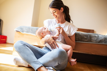 Mother sitting in bedroom and feeding her baby.	