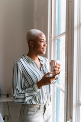 Happy woman with cell phone and coffee cup looking out of window