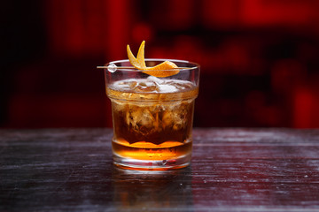 Food and drinks content. Closeup of a God father cocktail in short glass, gin, standing on the bar counter, isolated on a red light background.