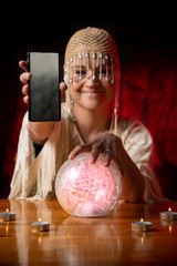 Fortune Teller with Crystal Ball and mobile phone on table with candles. Smartphone, online or call concept