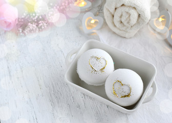 Fototapeta na wymiar Romantic spa set on white background. Close up bath bombs in ceramic bowl with hearts, towel on wooden desk. Bokeh effect. Copyspace.