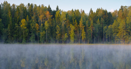 Morning fog on a lake in a fall forest. Beautiful landscape with reflection of trees
