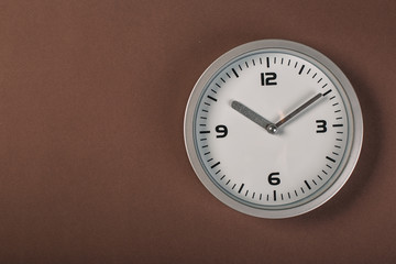 White wall clock with a yellow used hanging on the wall. Minimalist image of a wall clock on a brown background with copy space