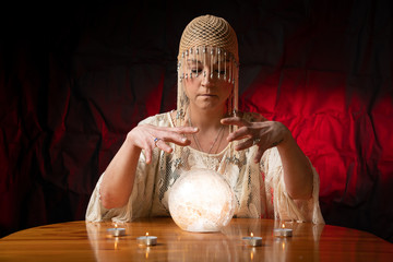 Fortune Teller with Crystal Ball on table with candles and black and red mottled background