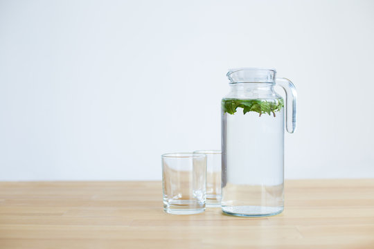 carafe with water and mint and several glass glasses on a wooden table with a light background