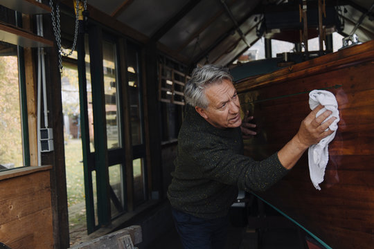 Senior man cleaning wooden boat in a boathouse