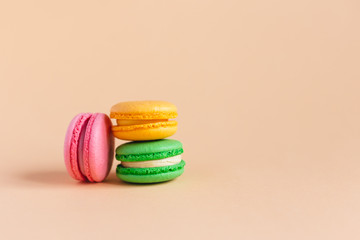 Three tasty french macarons on peach pastel background.  Pink, yellow and green macarons.