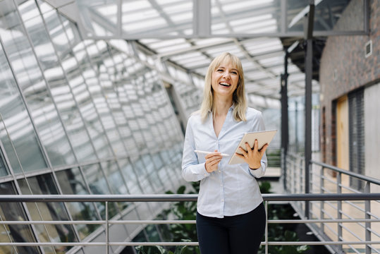 Laughing young businesswoman in a modern office building using tablet