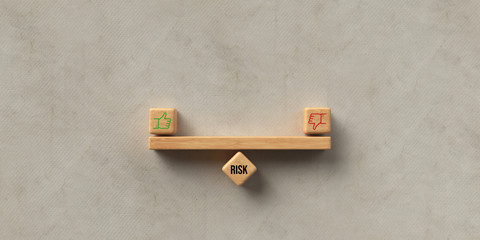 wooden blocks formed as a seesaw with the word RISK and thumb up and thumb down icon on paper...