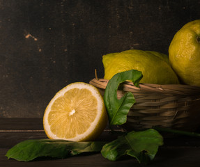 Detail of a cut lemon accompanied by other lemons in a basket and its green leaves. On a wooden...
