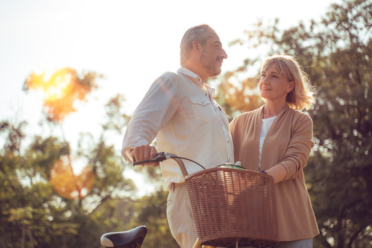 Beautiful Senior couple walking their bike along happily talking in park.mature couple in summer park.Elderly man and old woman with bicycles outside in spring nature.