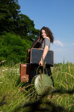Portrait of young woman on a meadow with many suitcases