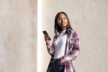 Fototapeta premium Portrait of African American young beautiful woman standing on the street while using a mobile phone