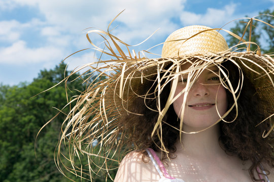 Portrait of smiling young woman wearing frayed straw hat in nature