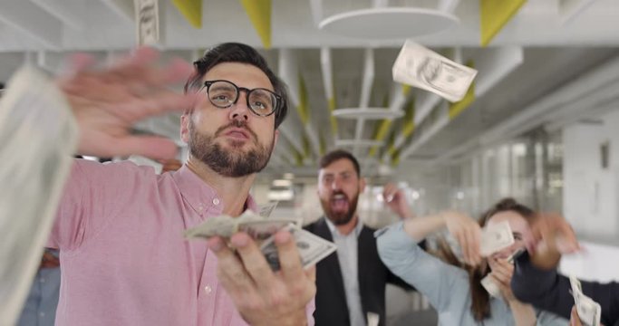 Excited businessman with team of mixed ethnic workers celebrating successful contract. Close up of office workers being happy, scattering and throwing money in modern office room.