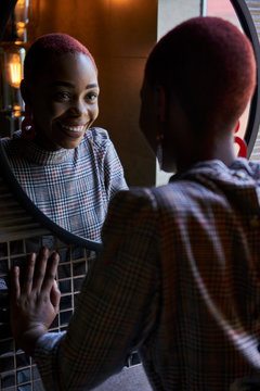 Young woman with short haircut looking and smiling to her reflection in a round mirror