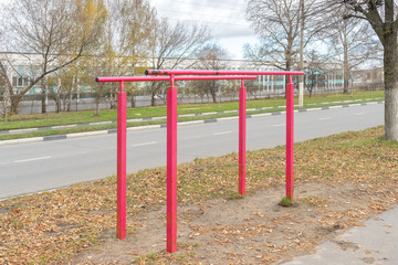 Fototapeta na wymiar Iron parallel bars with peeling red paint for pulling up are installed next to roadway. Sports equipment. Autumn landscape