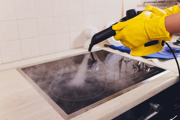 Cleaning kitchen hob with a steam cleaner.