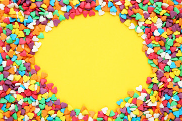Colorful heart shaped sprinkles on yellow background