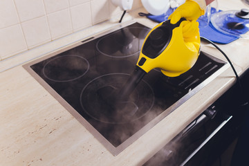 Cleaning kitchen hob with a steam cleaner.
