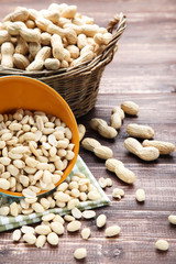 Peanuts in basket and bowl on brown wooden table