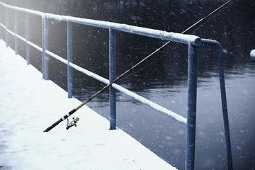 Old fishing pole leaning on handrail in winter