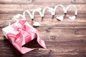 Gift box with ribbon and hearts on brown wooden table