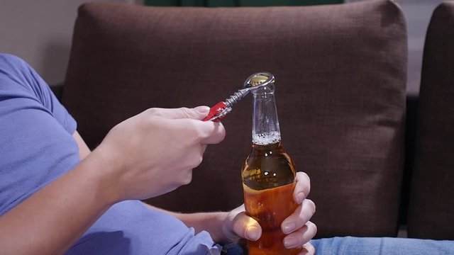 A man sitting on a sofa opens a bottle of beer