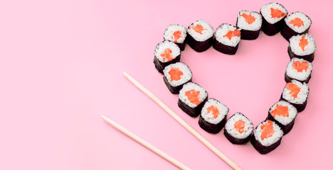 Salmon sushi rolls laid out in the shape of a heart on a pink background. The concept of Japanese cuisine for Valentine's Day, greeting card, banner. Copy space