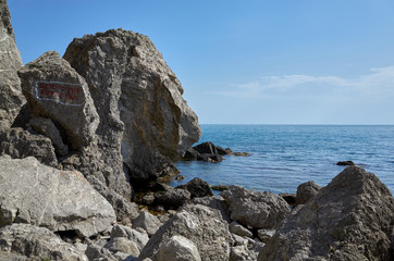The rocky coast of the Black Sea. Cape Alchak in Sudak, Crimea. The inscription on the rock "Caution rockfall"