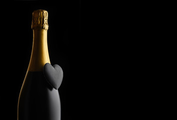 Closeup of a bottle of Champagne with a black heart against a black background with copy space.
