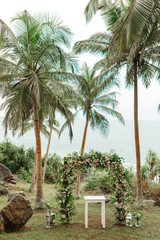 Fototapeta na wymiar Beautiful wedding arch on the tropical beach with palm trees. Beautiful beach wedding venue arrangement in nature in foreground coconut trees with panoramic ocean view