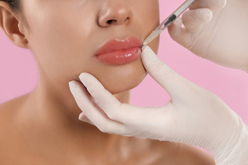 Young woman getting lips injection on pink background, closeup