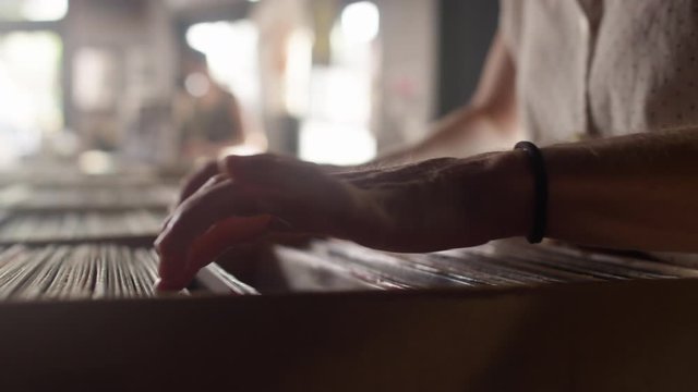 Close-up of a young woman's hands sifting through vinyl records in a record store