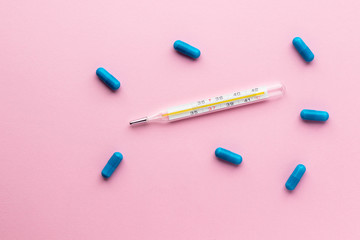 Mercury thermometer and blue pills isolated on pink background. Epidemic, painkillers, healthcare and treatment concept. Flat lay. Top view with copy space.