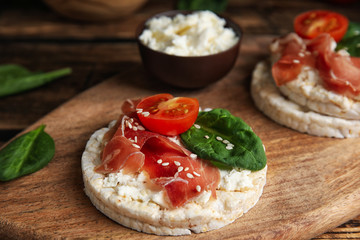 Puffed rice cake with prosciutto, tomato and basil on wooden board, closeup