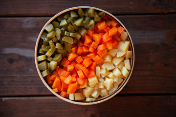 diced vegetables, carrots, potatoes, pickles. Top view on a wooden table.