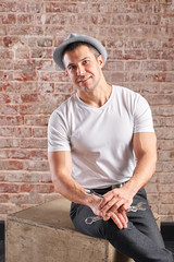 Athletic man with wrench on a brick background. Not a typical worker, in a white t-shirt and trousers.