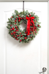 Beautiful red Christmas wreath of fresh spruce on the white door. Entrance to the house. Christmas mood. Xmas tree.