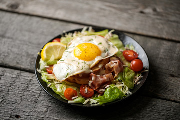 Croque-madame with salad on a black plate on a wooden background. 