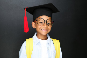 Young African American school boy in graduation cap with backpack on black background