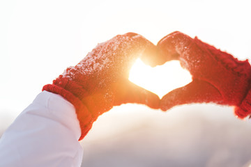 Woman making heart symbol with snowy hands in red gloves, sunny winterday, sun lights, Valentines day, Love concept.