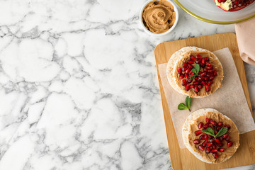 Puffed rice cakes with peanut butter and pomegranate seeds on white marble table, flat lay. Space...