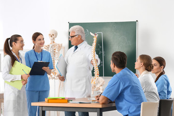 Medical students and professor studying human spine structure in classroom
